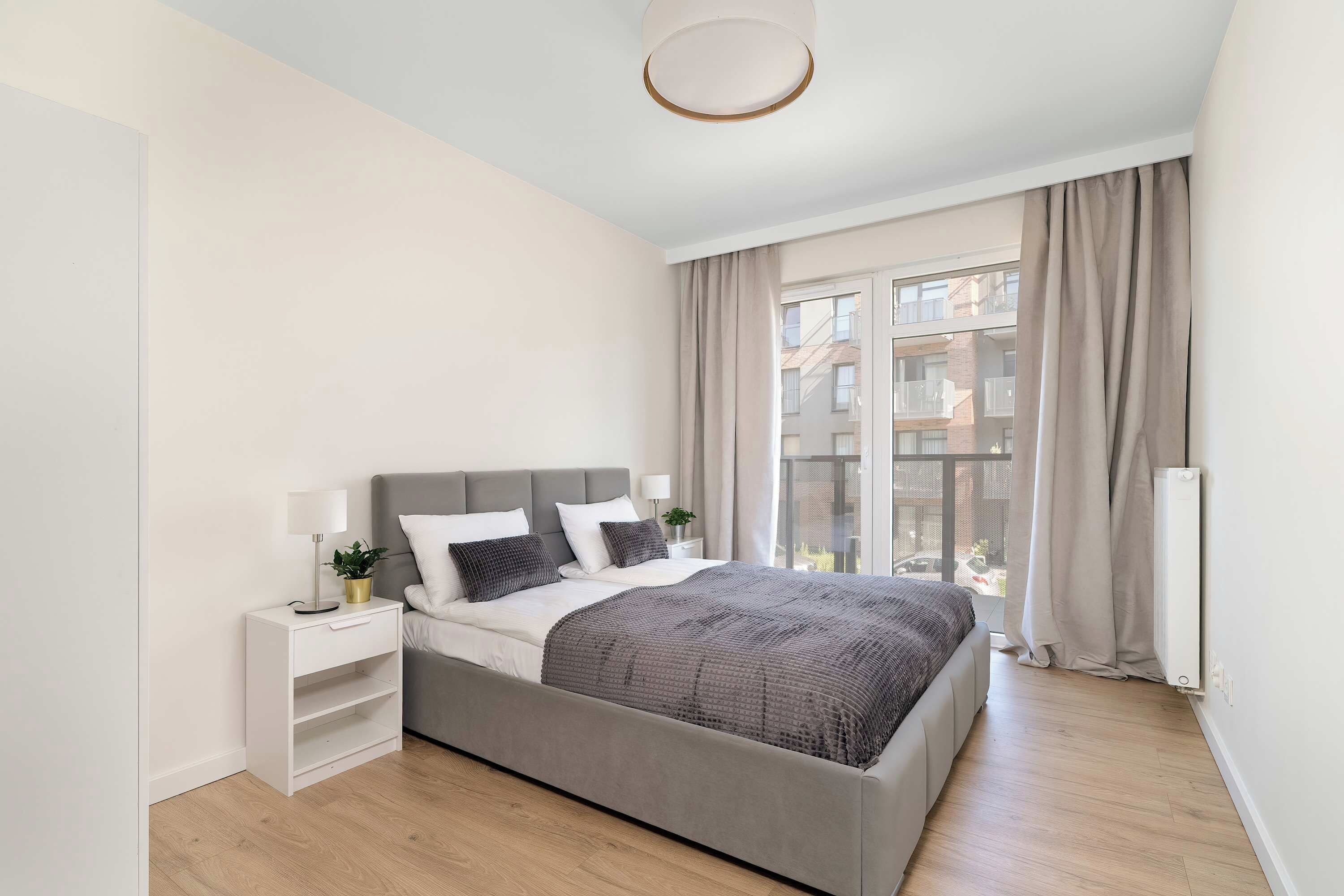 Un dormitorio moderno con una cama grande, mesitas de noche, una planta en maceta y vistas al exterior.