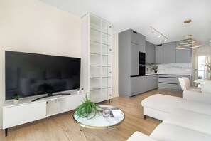 A modern living room with a flat-screen TV, a glass coffee table, and a white sofa. - Spacious Apartment with a balcony | Close to the Airport (Poznań)