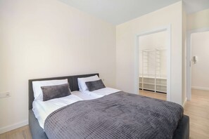 A bedroom with a bed, a wardrobe, and a door leading to another room. - Spacious Apartment with a balcony | Close to the Airport (Poznań)