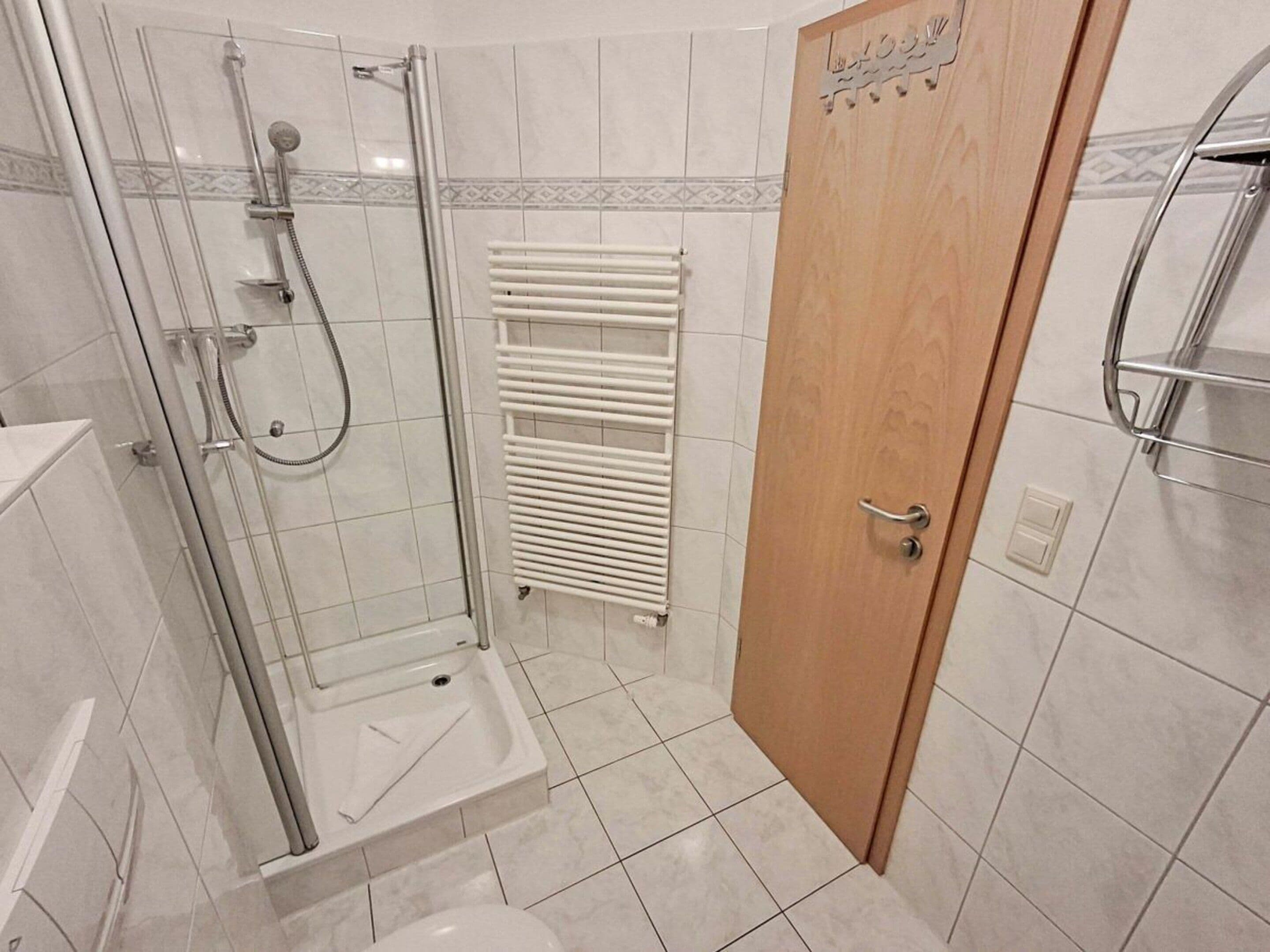 Ein Badezimmer mit einer gläsernen Duschkabine, einer weißen Toilette und einer Holztür.