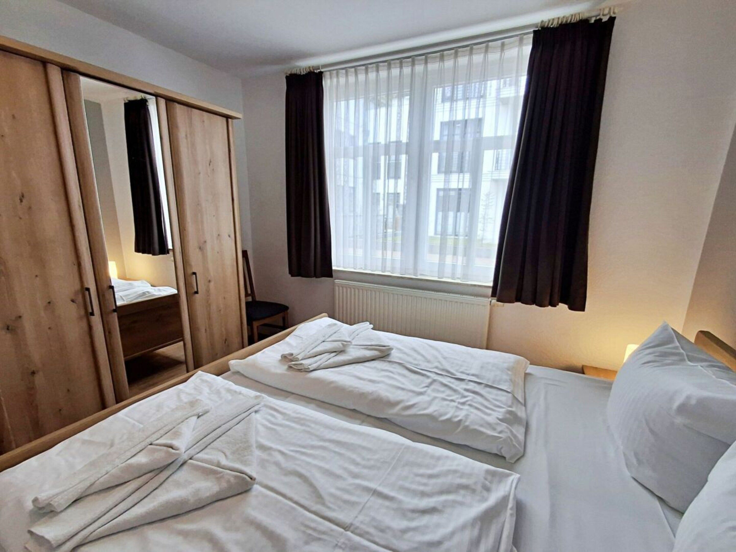 Une chambre d’hôtel avec deux lits, une armoire en bois, une fenêtre avec des rideaux et un radiateur.
