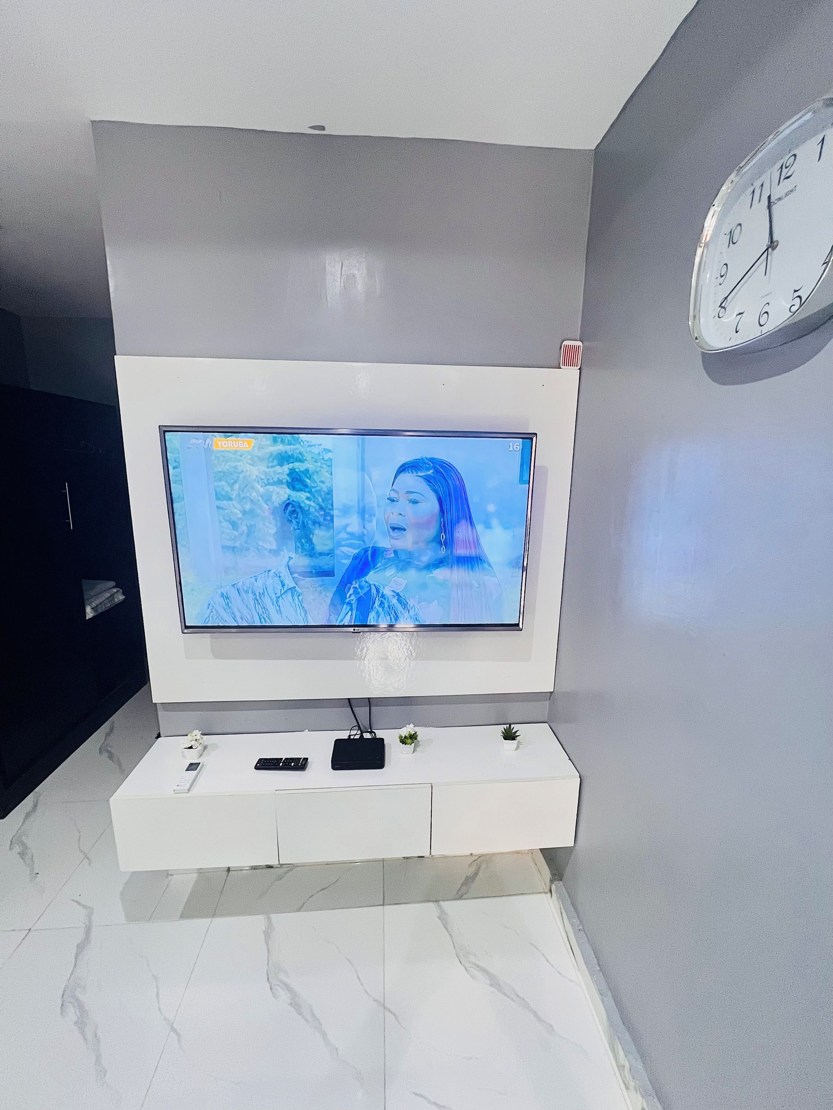 Un téléviseur à écran plat fixé à un mur blanc, avec une horloge au-dessus.