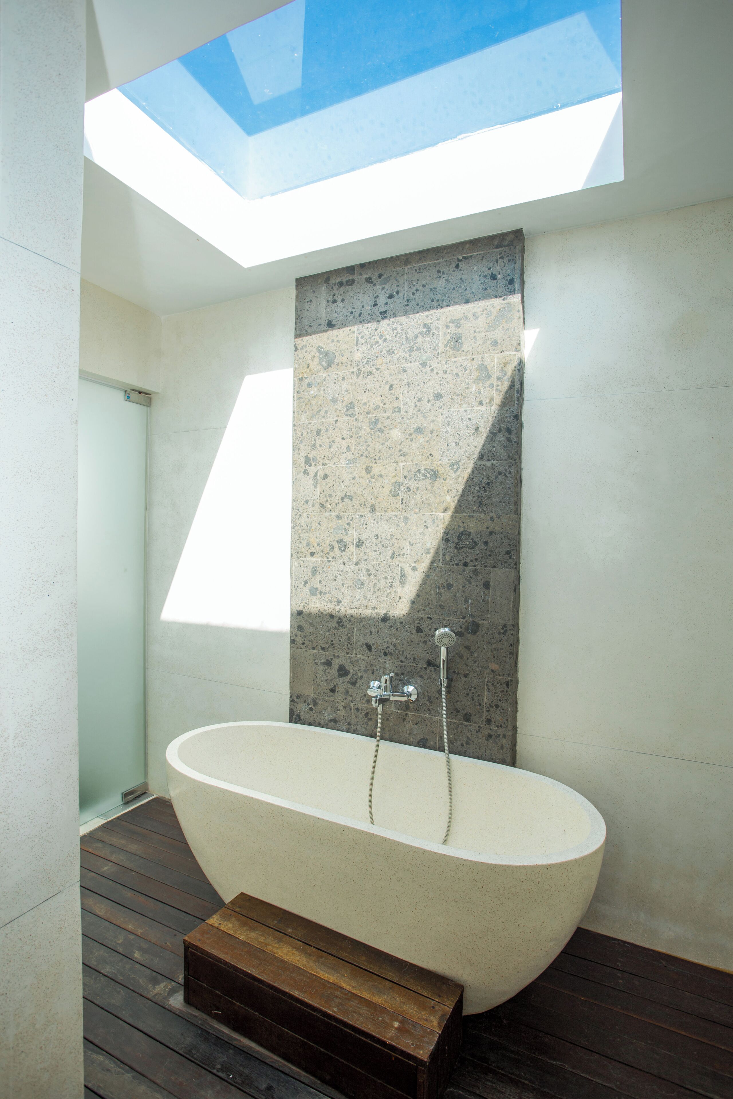 Un baño moderno con una bañera independiente, un tragaluz y una pared de acento de piedra.