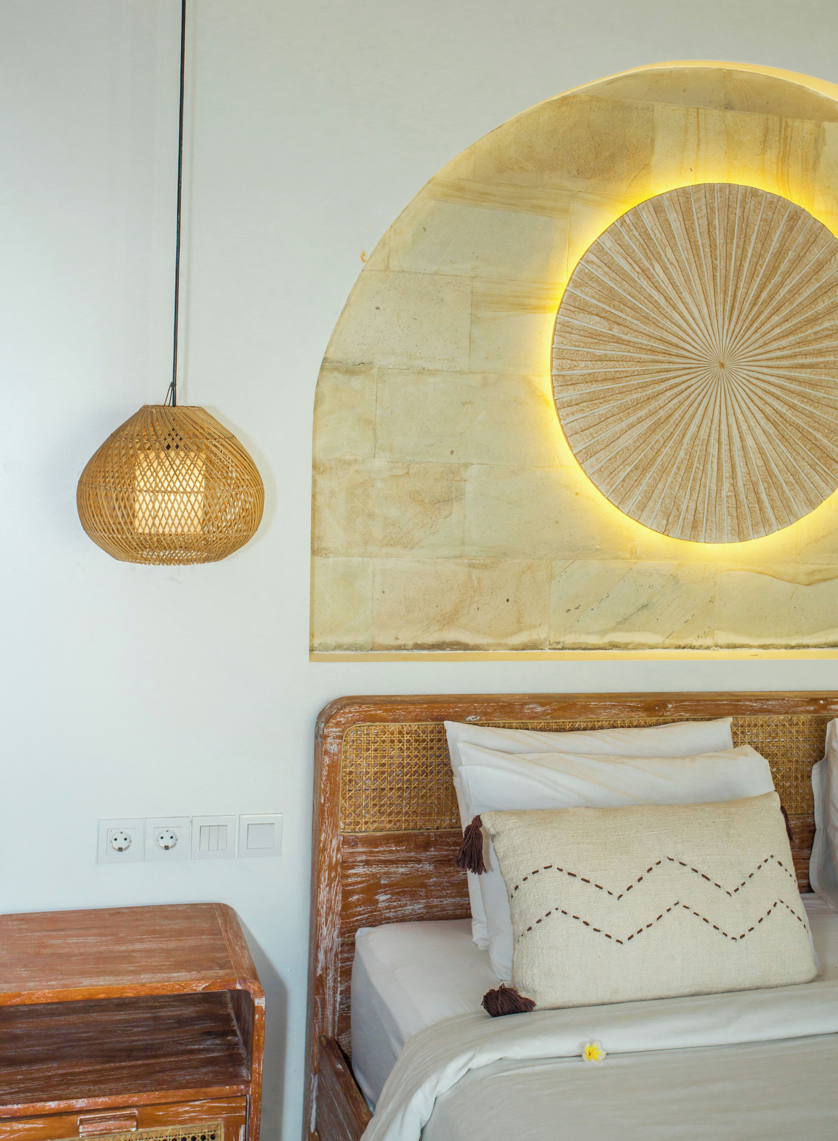 Una cama con cabecera, una lámpara colgante y una luz instalada en la pared.