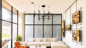 A modern living room with a white sofa, orange chair, and a coffee table. There are large windows and artwork on the walls. - One Studio Suite by PSH (Ou Chrov)