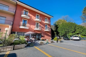 Un hotel de varios pisos con balcones, mobiliario exterior y un estacionamiento.