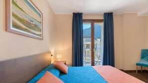 Hotellihuone, jossa on sänky, tuoli, parveke ja taulu seinällä.