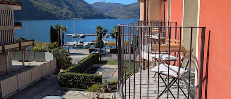 A balcony with a view of a lake and mountains, a parked car, and a building with a red facade.