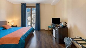 Hotellihuone, jossa on sänky, työpöytä, televisio ja näkymä ulkona oleviin rakennuksiin.