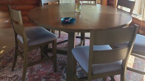 Un interior de madera con una mesa redonda, sillas, un reloj y vistas a través de una ventana.