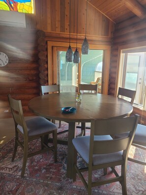 A wooden interior with a round table, chairs, a clock, and a view through a window. - Beachfront retreat on Sunset Beach (Oak Harbor)