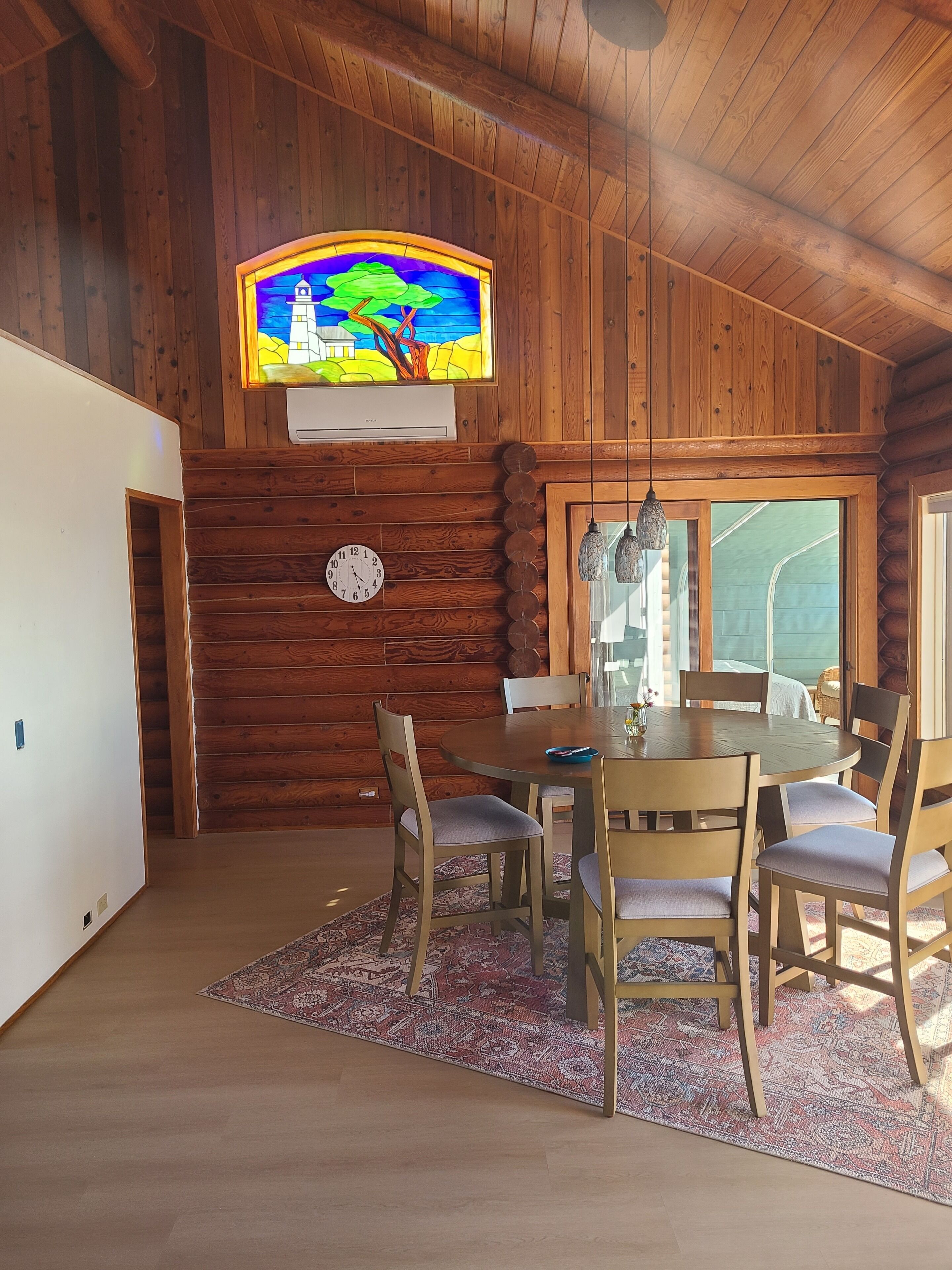 Ein Holzkamin mit Esstisch, Stühlen, einer Uhr und einem Buntglasfenster.