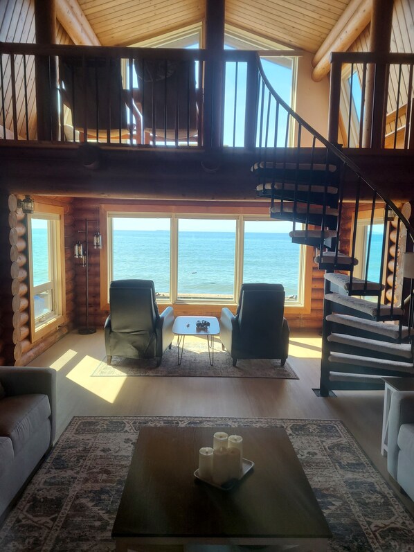 A log cabin interior with a view of the ocean, a staircase, and a seating area.