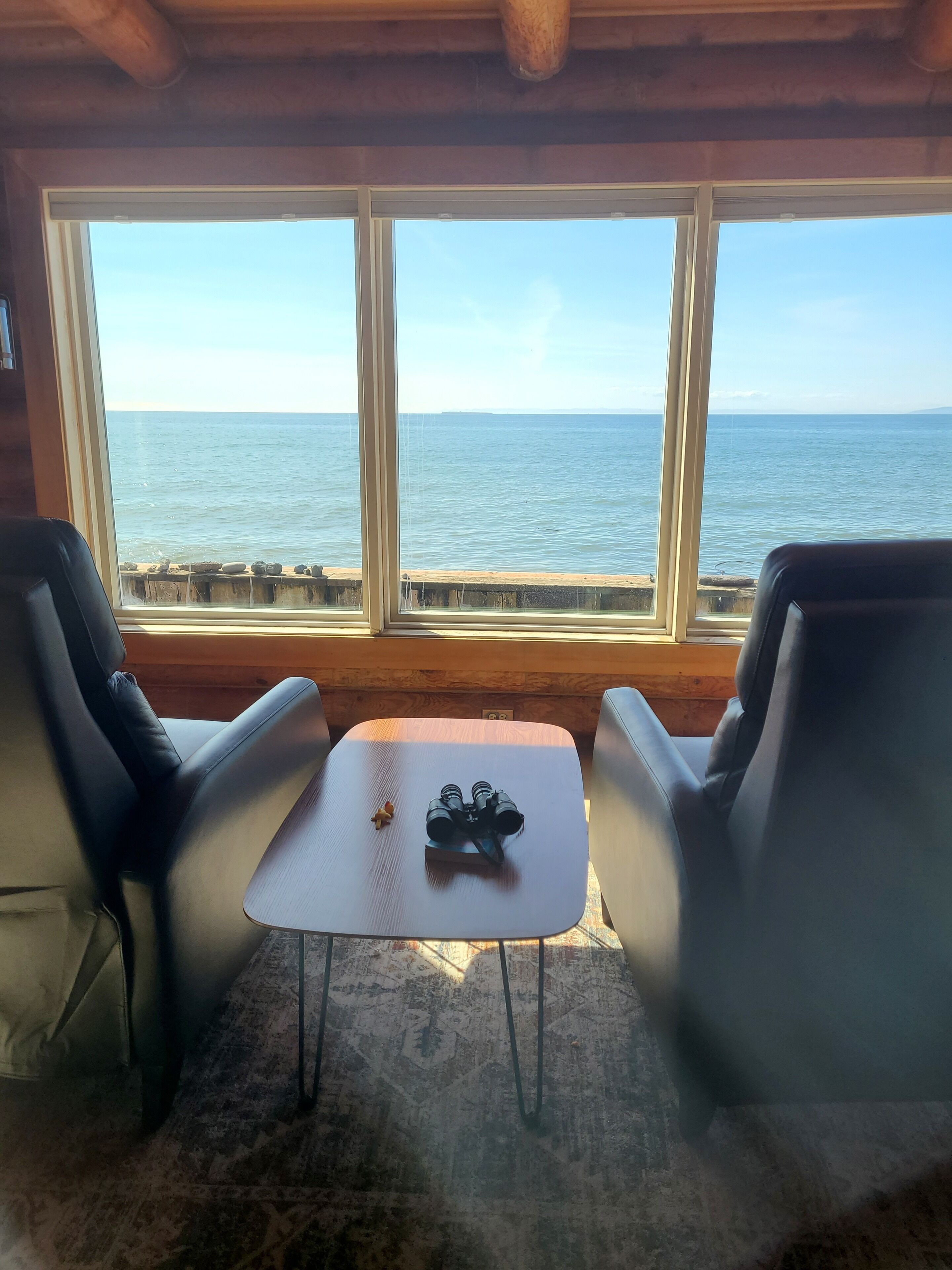 A room with a view of the sea, two leather chairs, a small table, and a pair of binoculars.