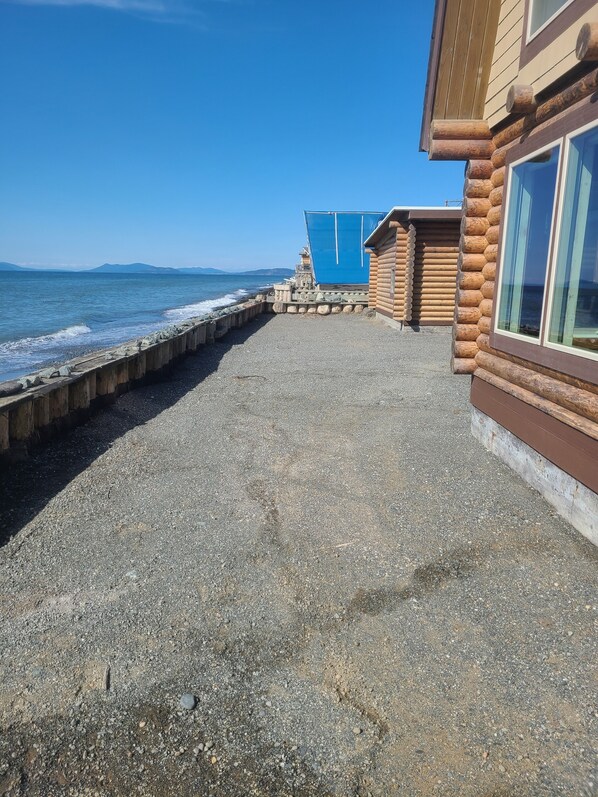 Un edificio de madera con ventanas amplias, un camino de grava y vista al mar.