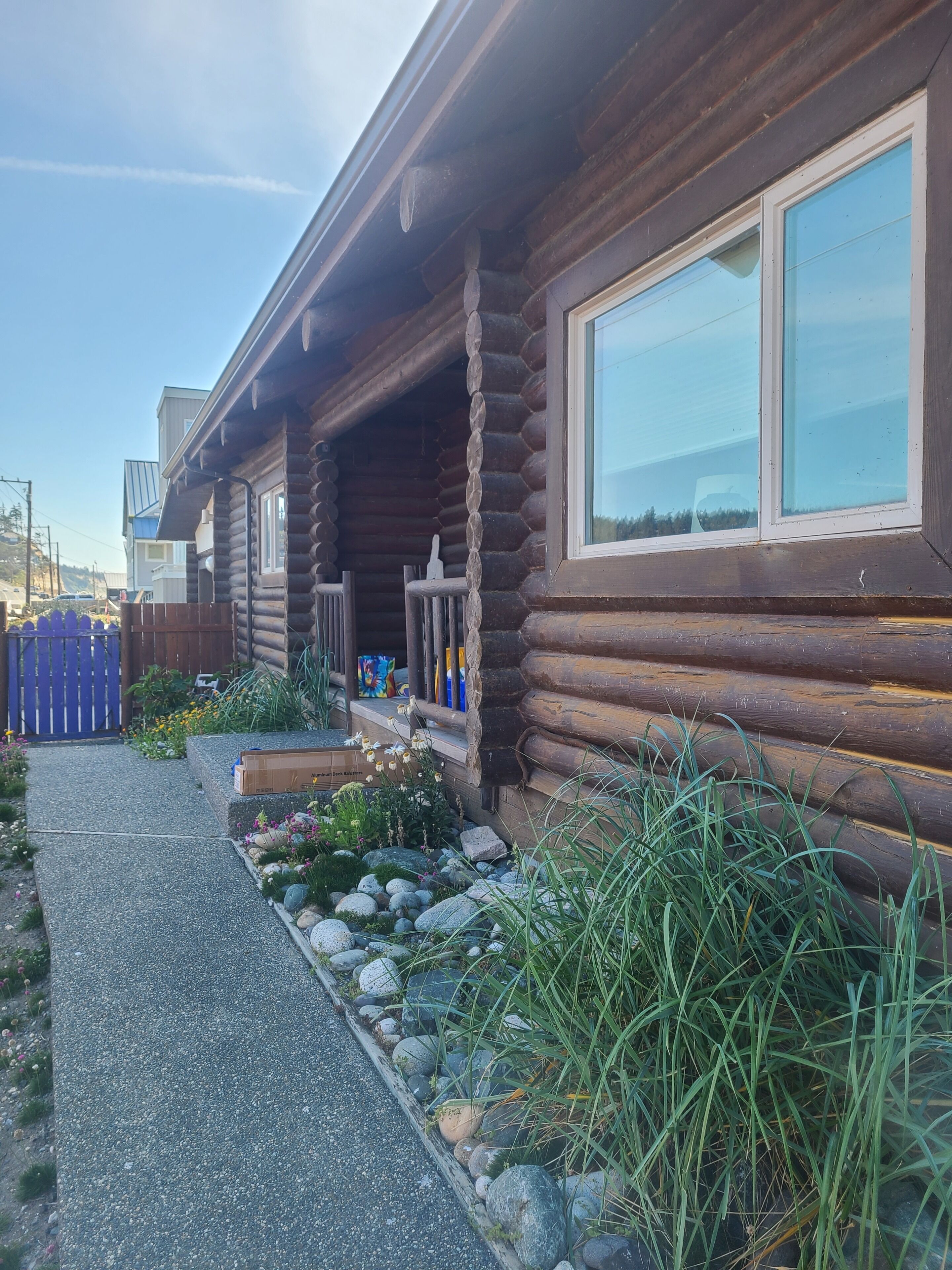 A log cabin with a porch, a window, and a garden with rocks and plants.