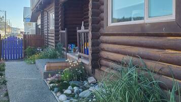 A log cabin with a porch, a window, and a garden with rocks and plants.