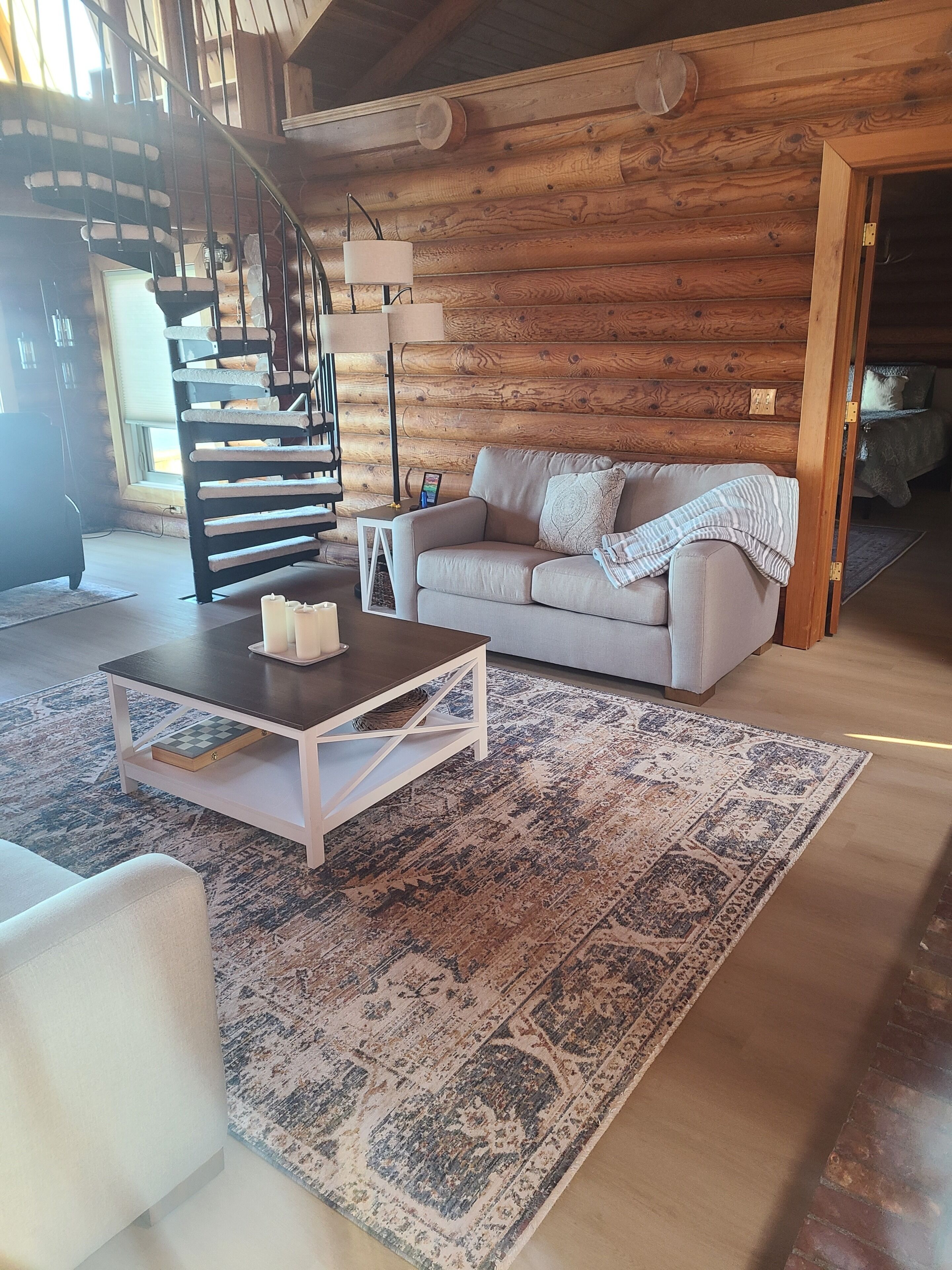 A log cabin interior with a staircase, a sofa, a coffee table, and a patterned rug.