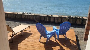 A wooden deck with two blue chairs and a table, overlooking a body of water.
