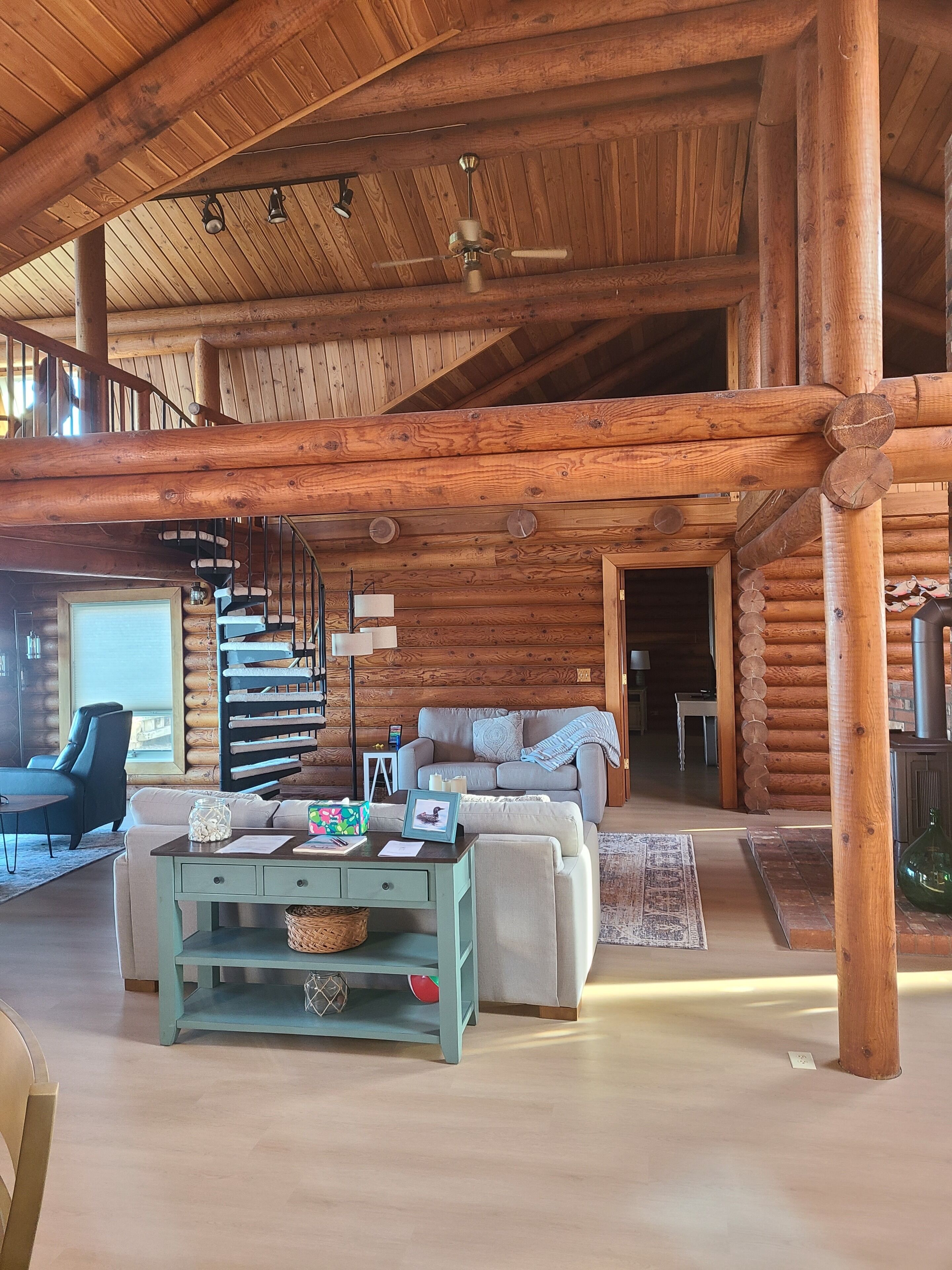 A spacious log cabin interior with a central seating area, a spiral staircase, and a fireplace.