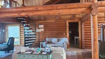 A spacious log cabin interior with a central seating area, a spiral staircase, and a fireplace.