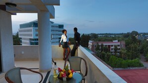 A balcony with two chairs, a table with a fruit basket and a bottle, and a view of buildings and greenery. - Rahnile Hotel (Bahir dar)