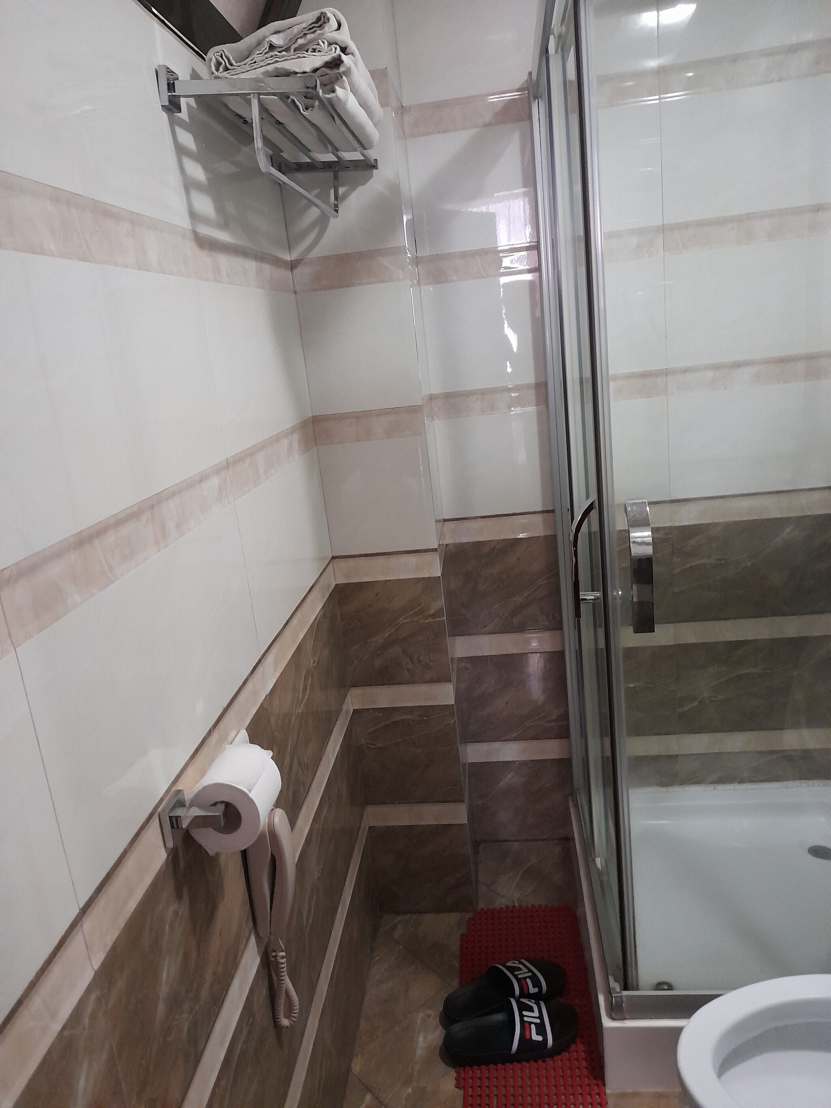 Casa de banho com cabine de chuveiro de vidro, sanita e suporte para toalhas.