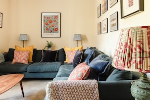 A living room with a dark green sofa, patterned cushions, a small table, and a lamp. - Russell Bank is a beautiful house with amazing sea views in the heart of Elie. (Elie and Earlsferry)