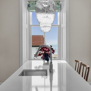 A kitchen with a white countertop, a stainless steel sink, and a view of the beach through a window. - Russell Bank is a beautiful house with amazing sea views in the heart of Elie. (Elie and Earlsferry)