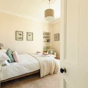 A bedroom with a bed, a bedside table, a chair, a shelf with books, and framed pictures on the wall. - Russell Bank is a beautiful house with amazing sea views in the heart of Elie. (Elie and Earlsferry)
