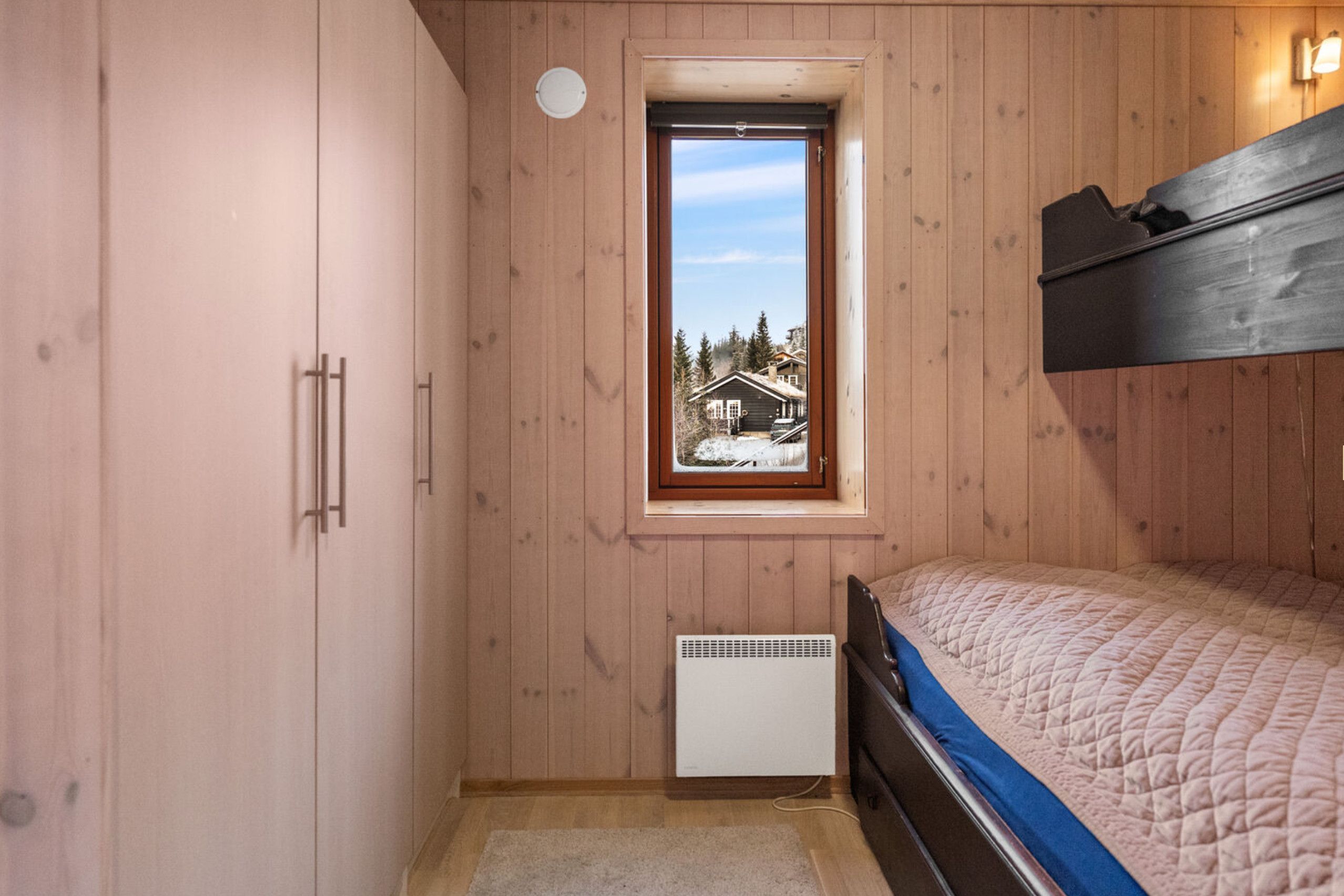 Una camera da letto con pareti in legno, una finestra vista casa, un letto, un termosifone e un armadio.