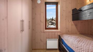 Una camera da letto con pareti in legno, una finestra vista casa, un letto, un termosifone e un armadio.