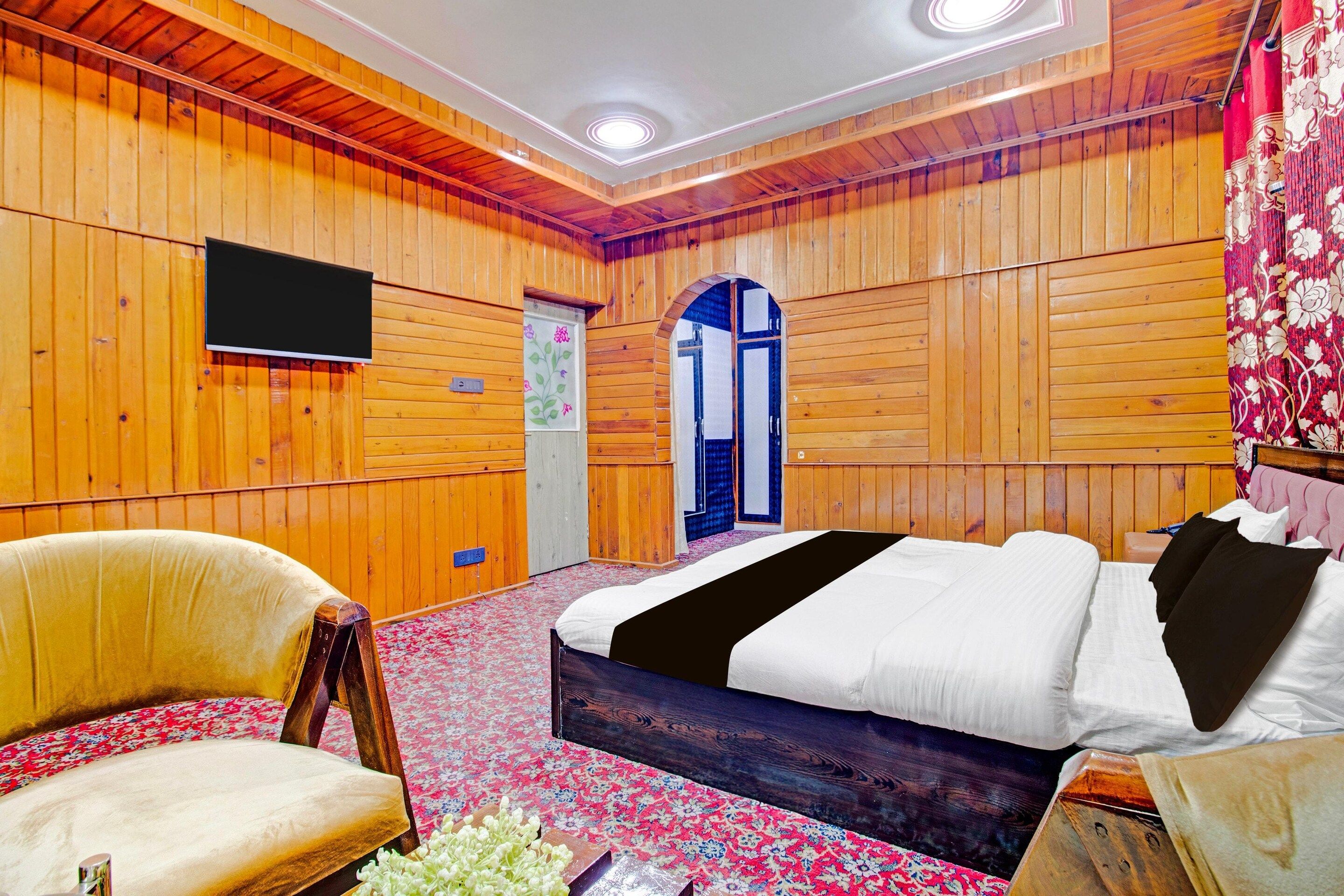 Quarto com painéis de madeira, uma cama, uma cadeira e uma televisão.