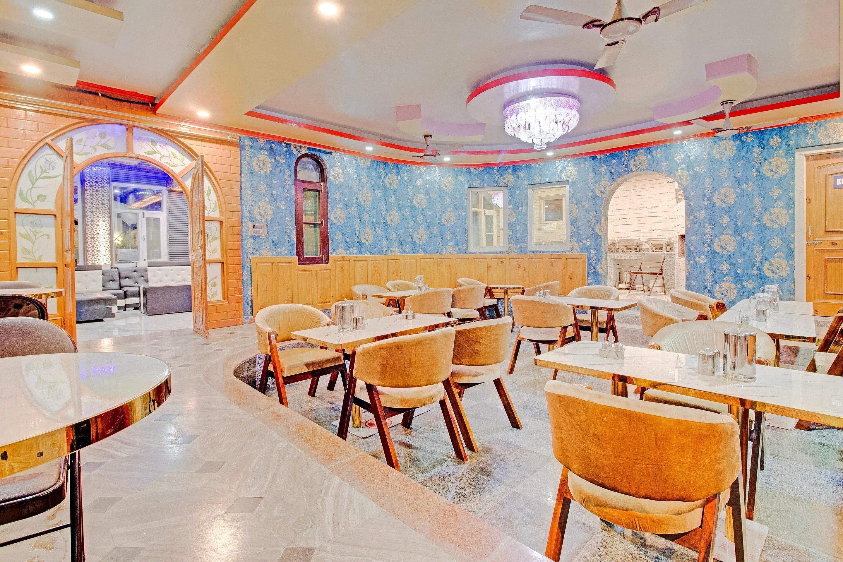 A restaurant with multiple tables and chairs, a chandelier, and patterned wallpaper.