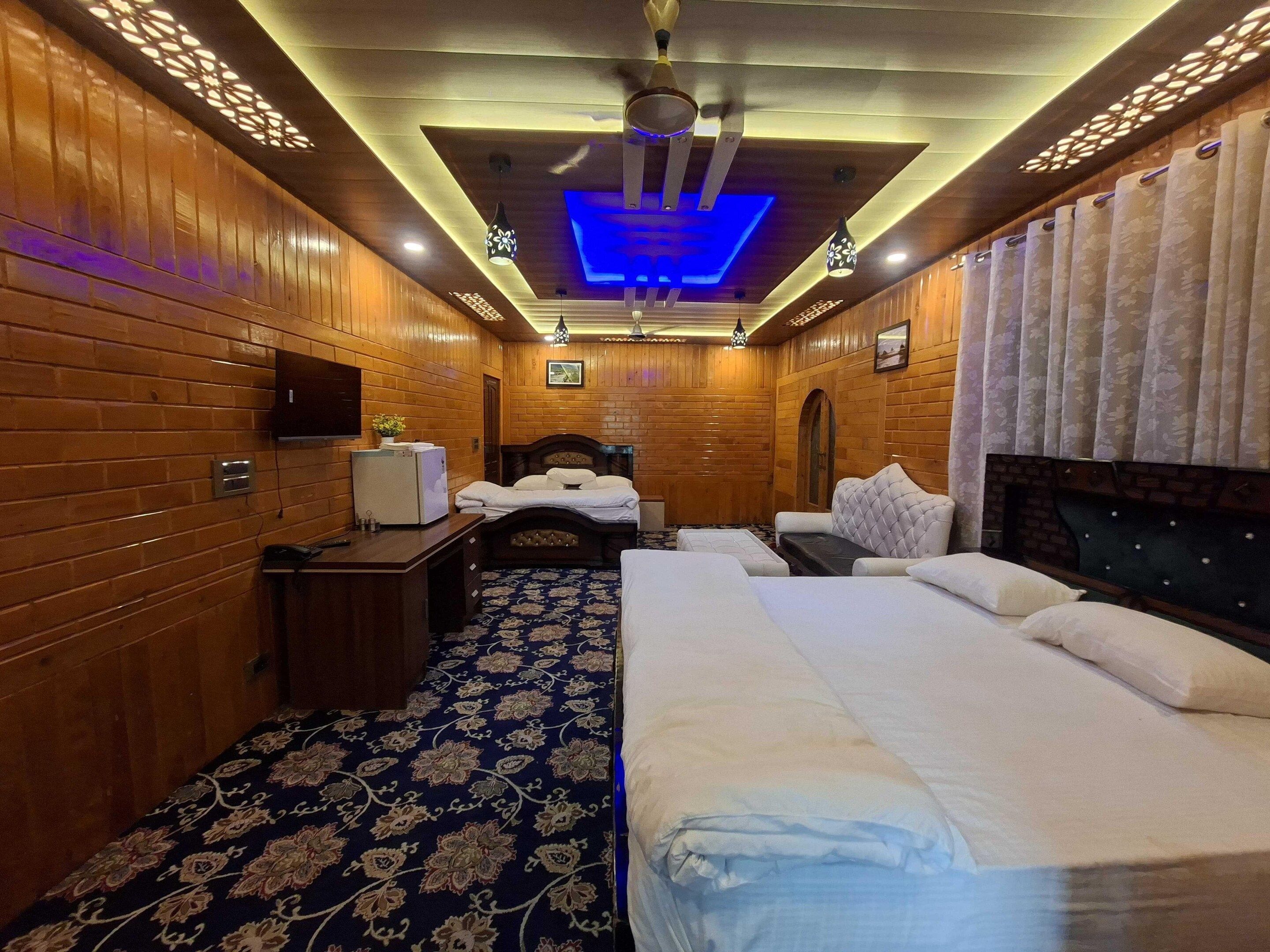 A hotel room with wooden paneling, a bed, a desk, a television, and a patterned carpet.