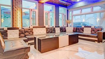 A spacious seating area with a mix of sofas and armchairs, a glass coffee table, and large windows offering a view of the outside.