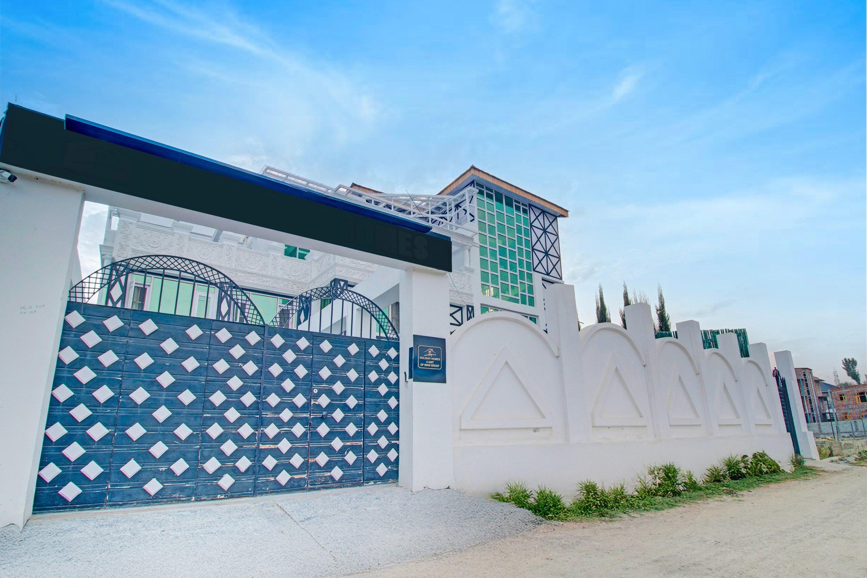 A gated property with a decorative metal gate, a white wall with a triangular design, and a sign indicating 'Holiday Homes A Unit Road.'