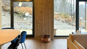 Une pièce spacieuse avec un intérieur en bois, de grandes fenêtres, une table à manger avec des chaises et un canapé.