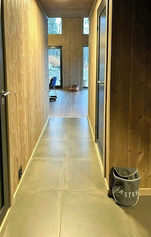 Ein Korridor mit Holzwänden und Fliesenboden, der zu einem Raum mit einem großen Fenster führt.
