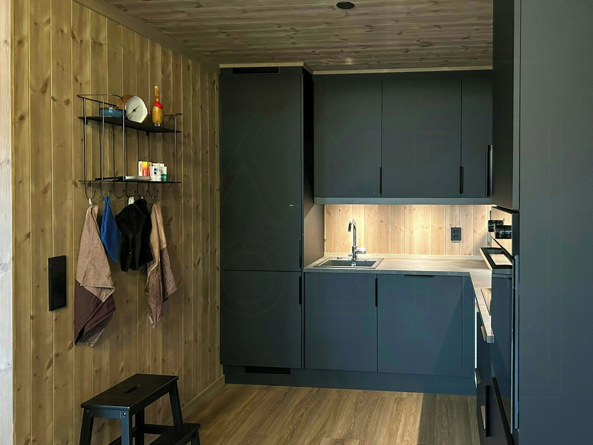 Eine kleine Küche mit dunklen Schränken, einer Holzwand und einem kleinen Hocker.
