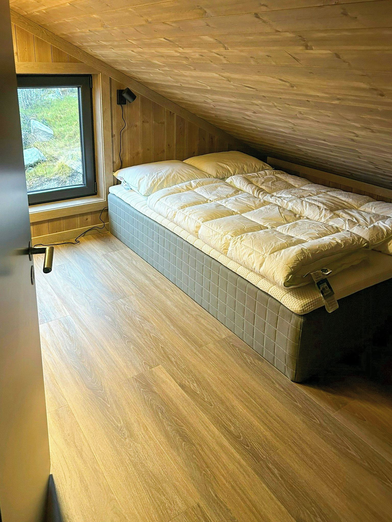 Ein kleines Schlafzimmer mit einem Einzelbett, Holzboden und einem Fenster mit Blick auf Grünflächen.