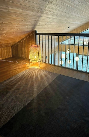 Ein Zimmer mit schrägen Wänden, einem gemusterten Teppich, einem Sessel und einem Fenster mit Blick.