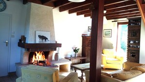 A cozy living room with a fireplace, wooden beams, a clock, and a yellow armchair. - Lovely Holiday Home in Sarzeau for 8 (Sarzeau)