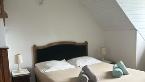 A bedroom with a sloped ceiling, a bed with white linens, two bedside lamps, and a wooden nightstand. - Lovely Holiday Home in Sarzeau for 8 (Sarzeau)