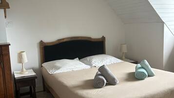 A bedroom with a sloped ceiling, a bed with white linens, two bedside lamps, and a wooden nightstand.