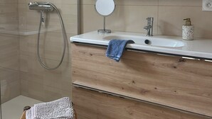 A modern bathroom with a glass shower enclosure, a wooden vanity with a mirror, and a small wicker stool. - Lovely Holiday Home in Sarzeau for 8 (Sarzeau)