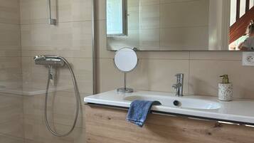 A modern bathroom with a glass shower enclosure, a wooden vanity with a mirror, and a small wicker stool.