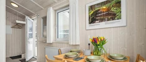 Un coin repas avec une table en bois dressée pour deux personnes, un tableau représentant une cascade accroché au mur et un vase de tulipes posé sur la table.