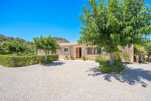 A stone house with a tiled roof, surrounded by gravel, trees, and a hilly landscape. - Villa Malagarba - By Dream Villas Pollensa (Pollensa)