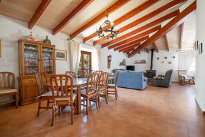 A dining area with wooden chairs and a table, a living room with a blue sofa, and a kitchen area with a stove. - Villa Malagarba - By Dream Villas Pollensa (Pollensa)